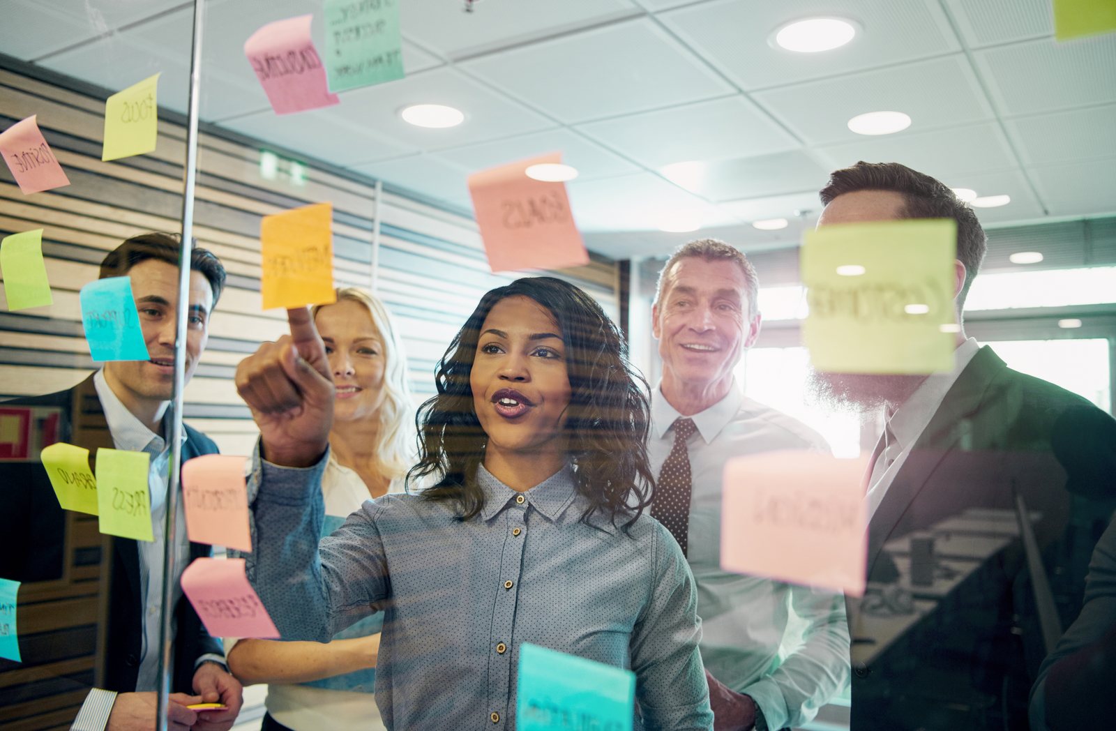 A team collaborating at a glass wall covered in sticky notes, mapping out ideas together